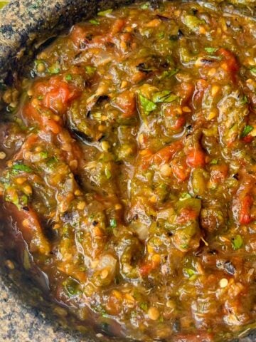 Molcajete salsa in a large molcajete with chips and lime wedges on the side.