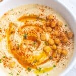 Homemade hummus in a bowl with extra-virgin olive oil drizzled over and topped with chickpeas, paprika, and chopped parsley.