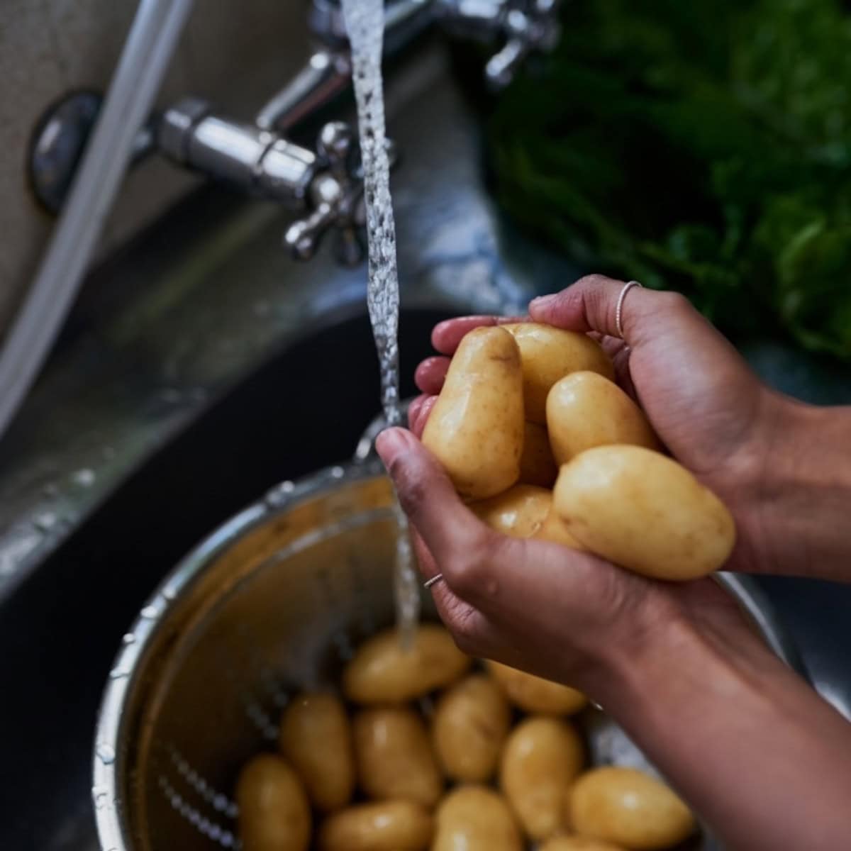 A person rinsing potatoes with water in a sink.
