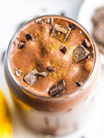 A banana cocoa peanut butter smoothie in a glass topped with chocolate chunks.