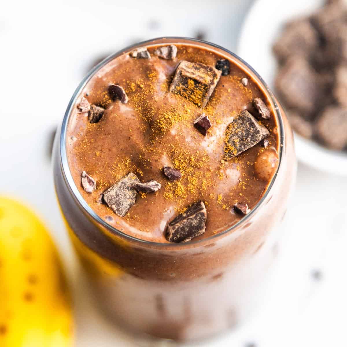 A banana cocoa peanut butter smoothie in a glass topped with chocolate chunks.
