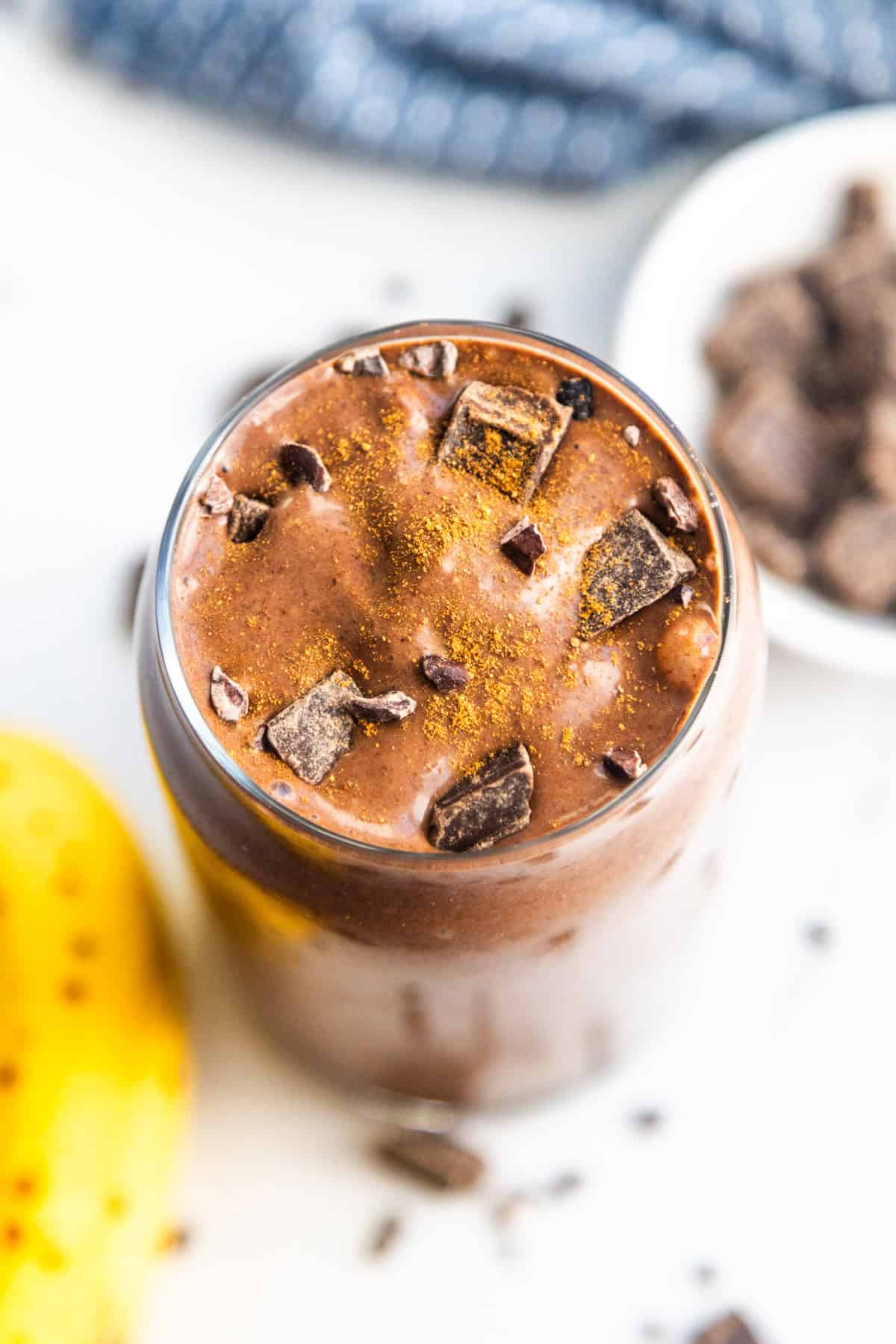 Banana cocoa peanut butter smoothie in a glass topped with chocolate chunks.