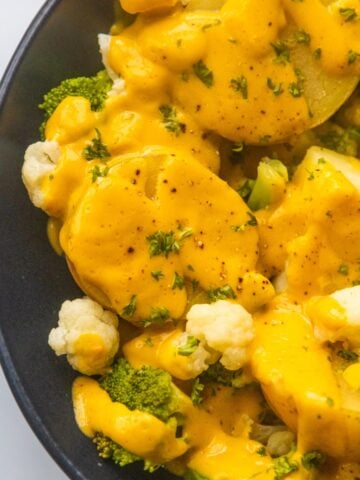 Vegan cheesy broccoli and cauliflower potatoes in a black bowl.