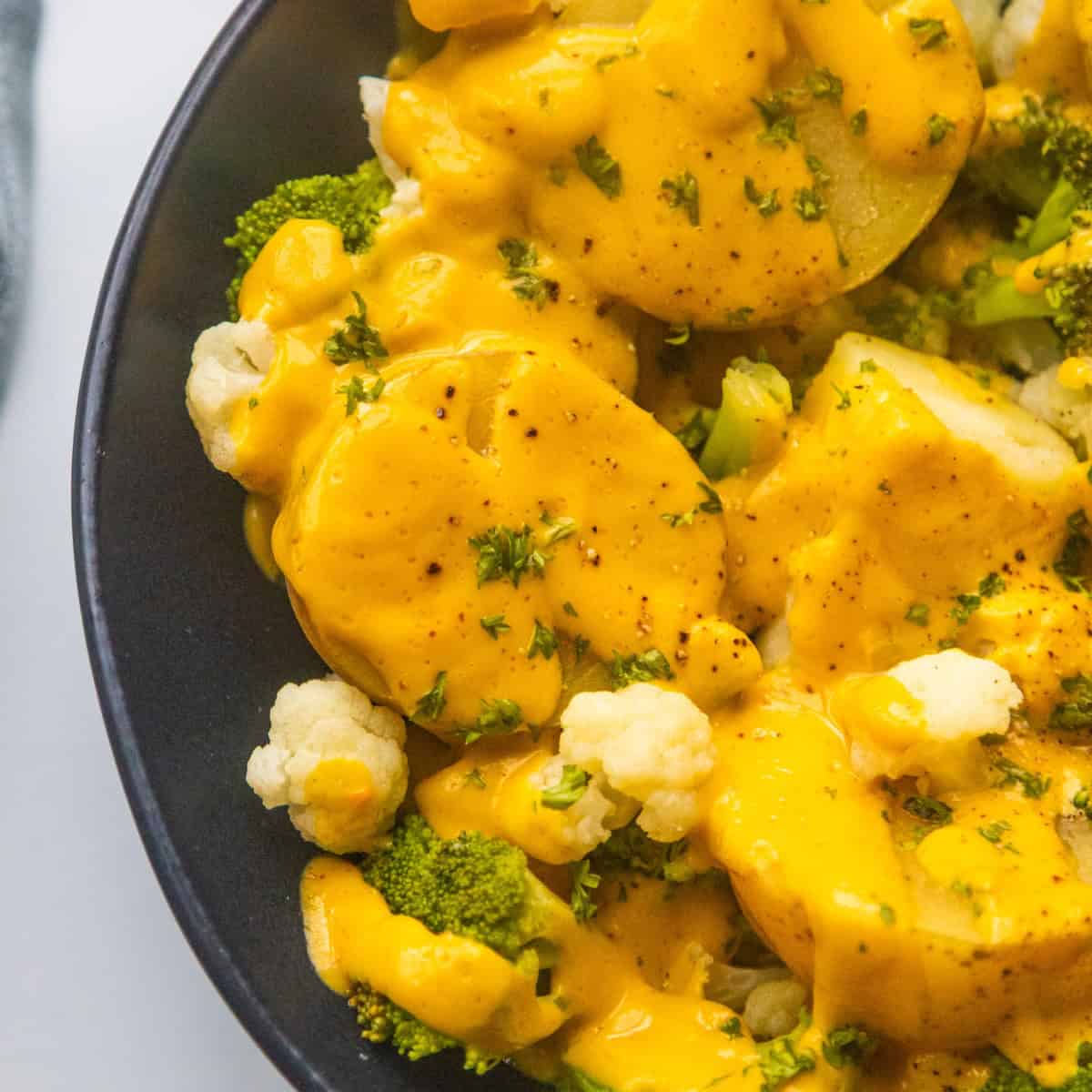Vegan cheesy broccoli and cauliflower potatoes in a black bowl.