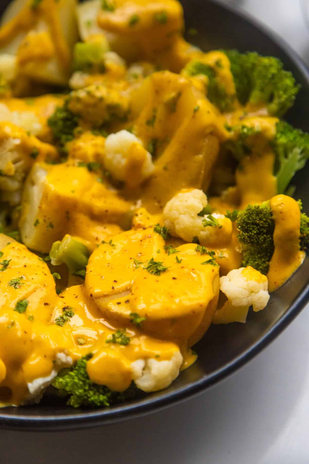 Vegan cheesy broccoli and cauliflower potatoes in a bowl topped with black pepper and chopped parsley.