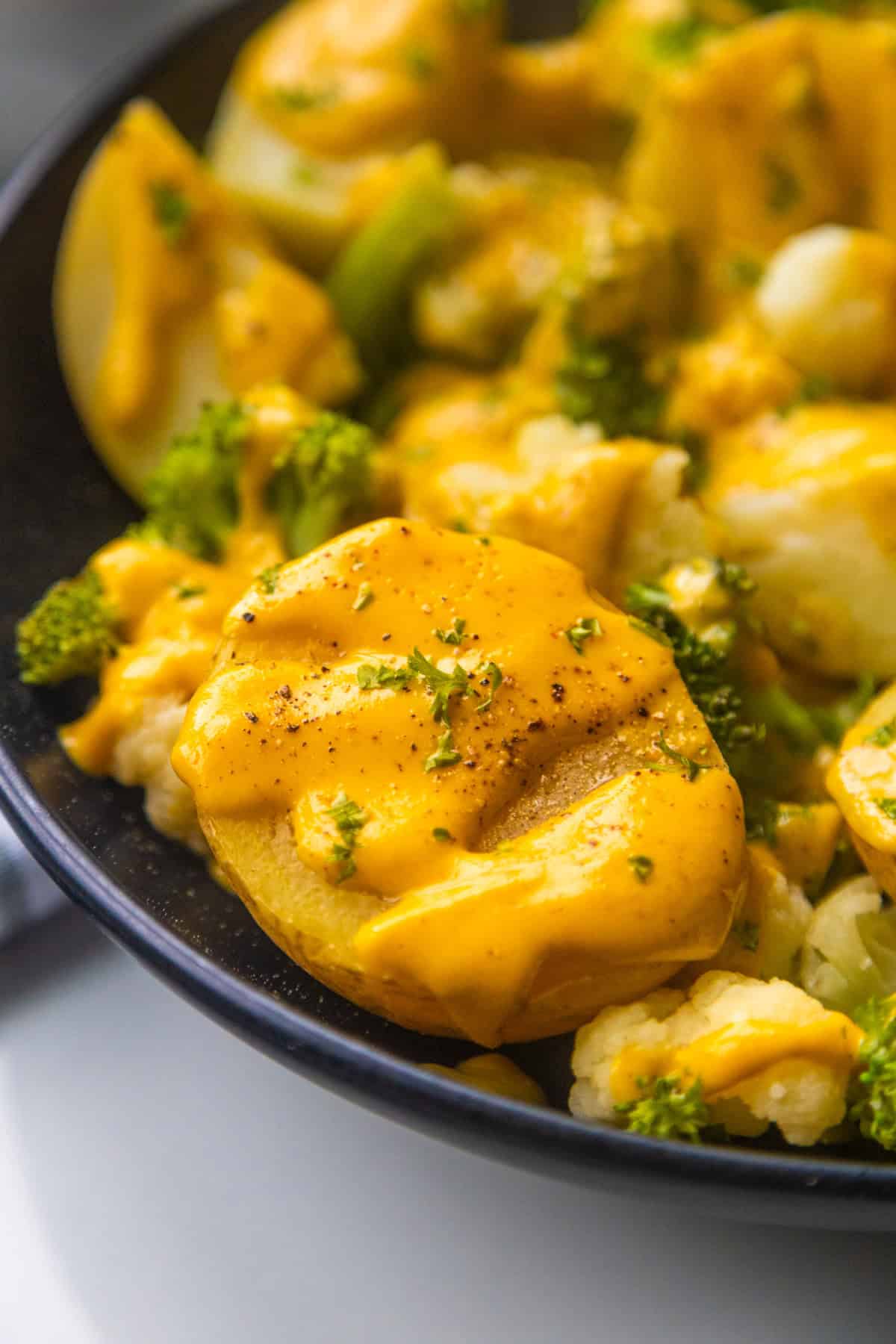 Vegan cheesy broccoli and cauliflower potatoes in a serving bowl topped with chopped parsley.