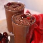 Red emerald chocolate bliss smoothie in a glass topped with cacao nibs and cherries.