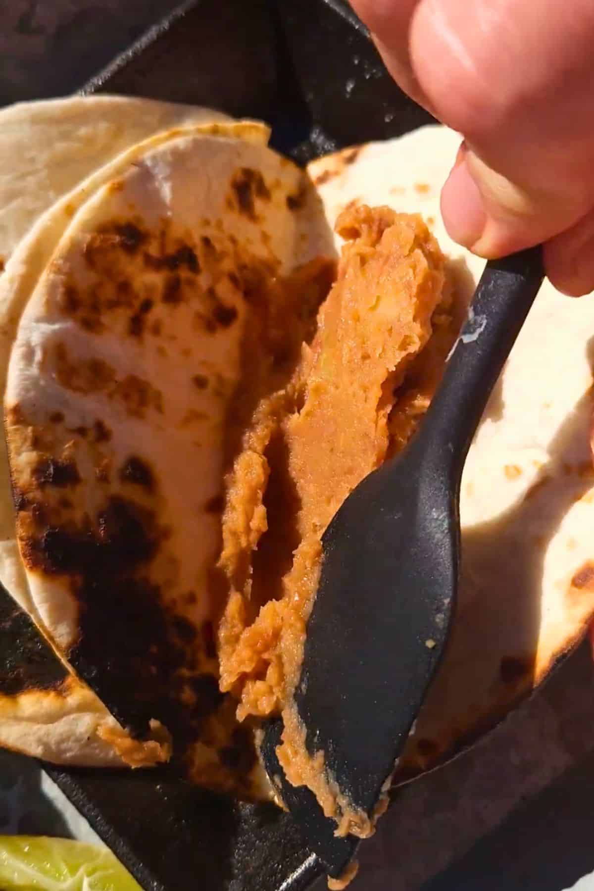 Refried beans spreading onto a tortilla.