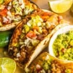 Tacos with refried beans and rice on a wooden cutting board with lime wedges on the side.