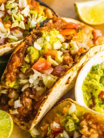 Tacos with refried beans and rice on a wooden cutting board with lime wedges on the side.