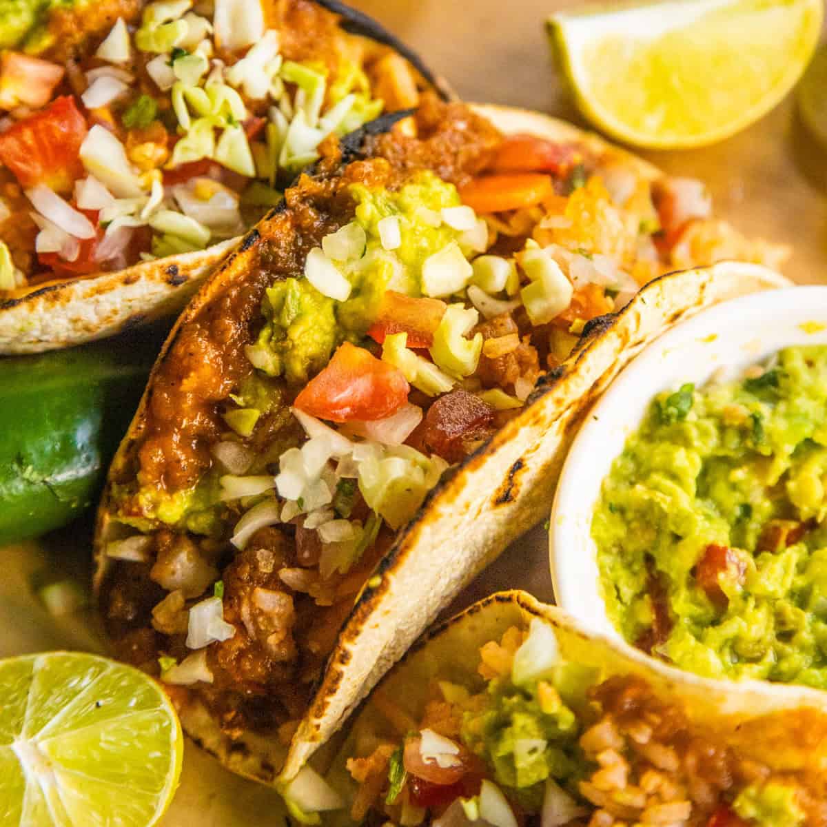 Tacos with refried beans and rice on a wooden cutting board with lime wedges on the side.