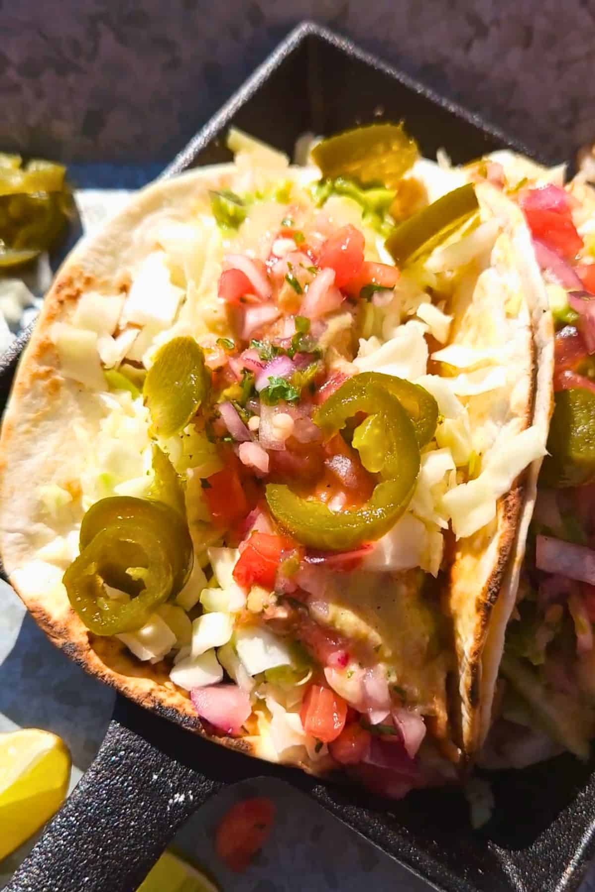 Tacos with refried bans and rice on a plate topped with pickled jalapeños.
