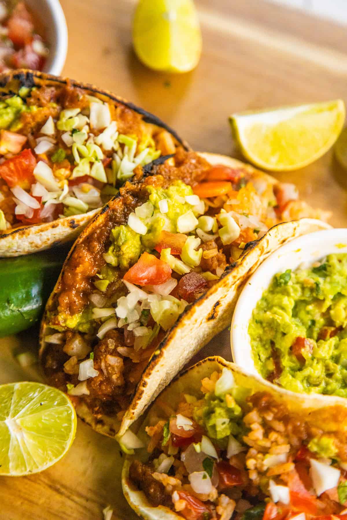 Tacos with refried beans and rice on a wooden cutting board with lime wedges on the side.