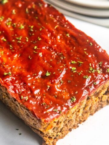 A sliced loaf of vegan meatloaf garnished with fresh parsley on a white board.