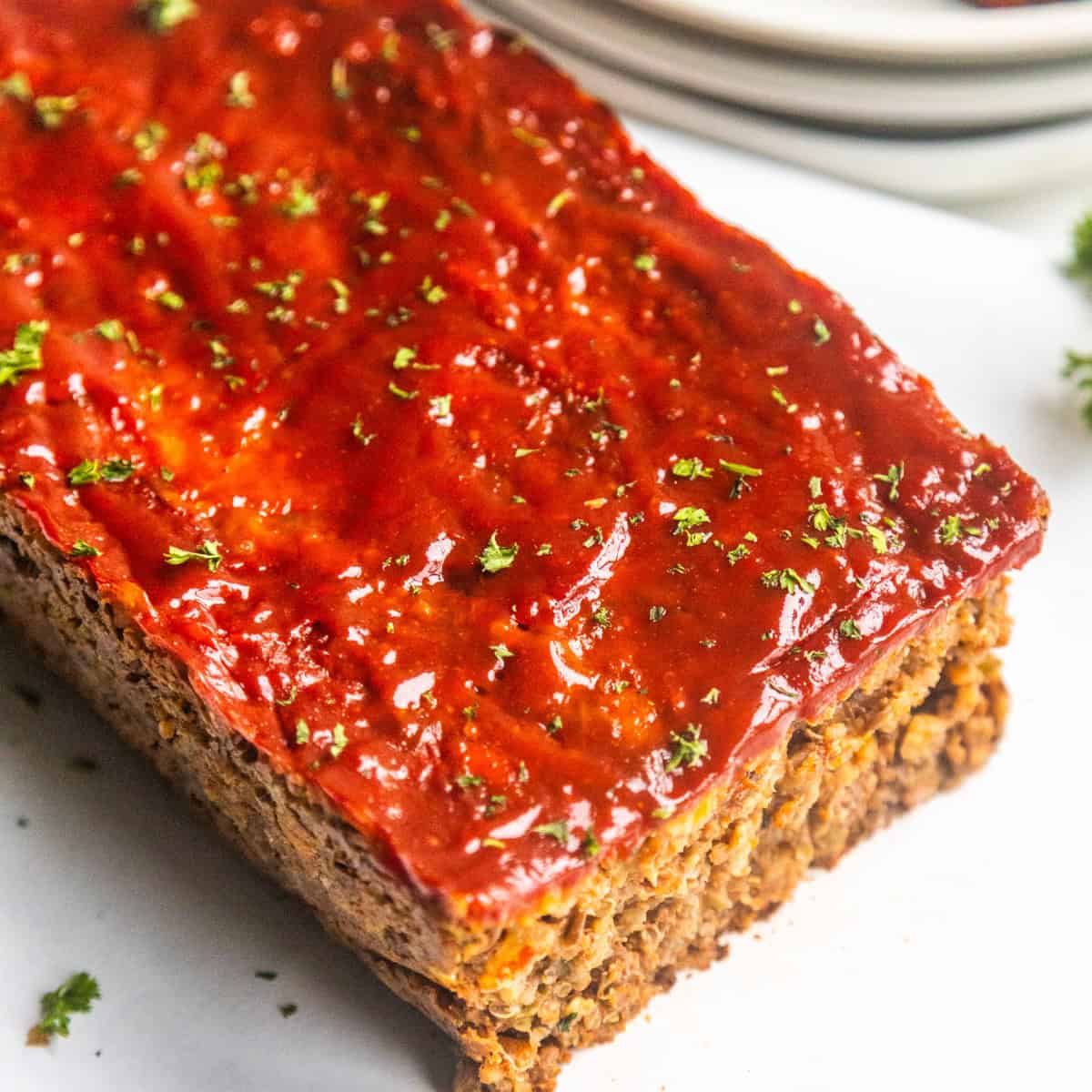 A sliced loaf of vegan meatloaf garnished with fresh parsley on a white board.