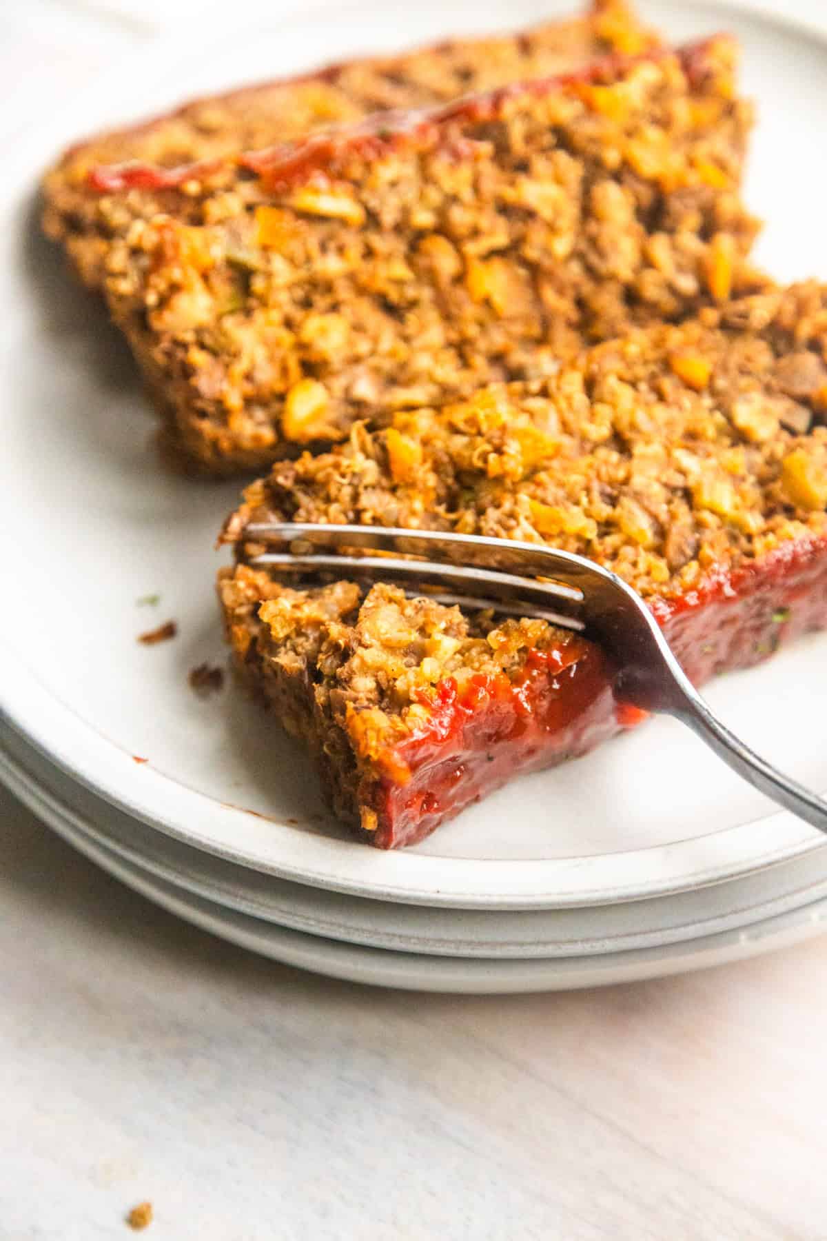Slice of vegan meatloaf on a plate being cut with a fork.