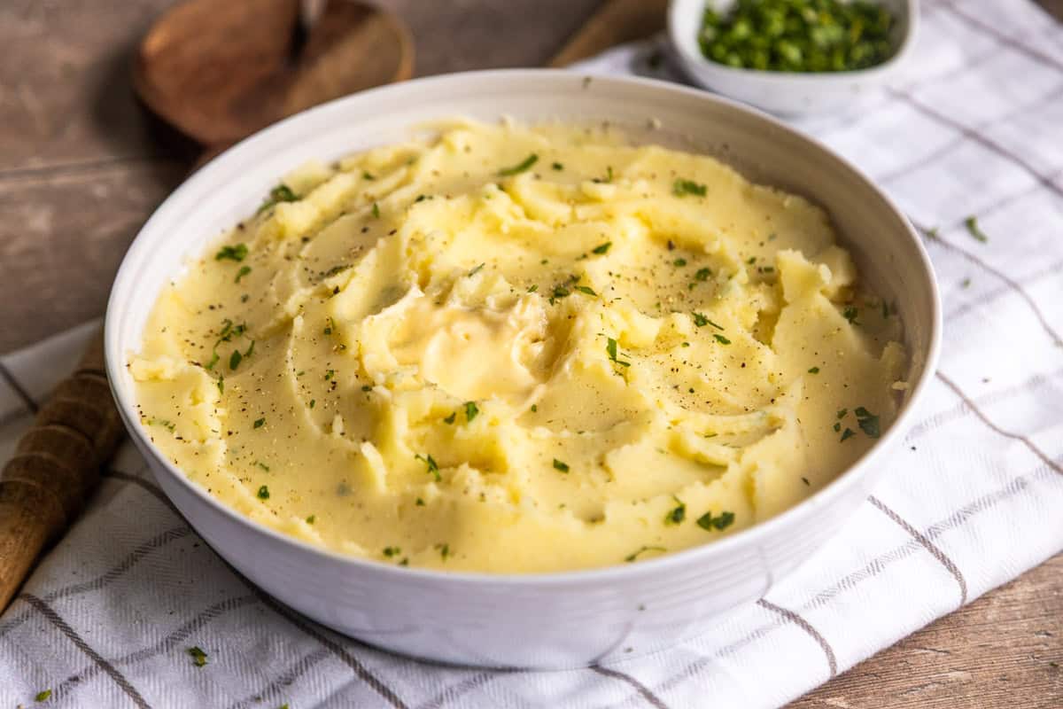 Creamy vegan mashed potatoes in a white bowl with a wooden spoon on the side.