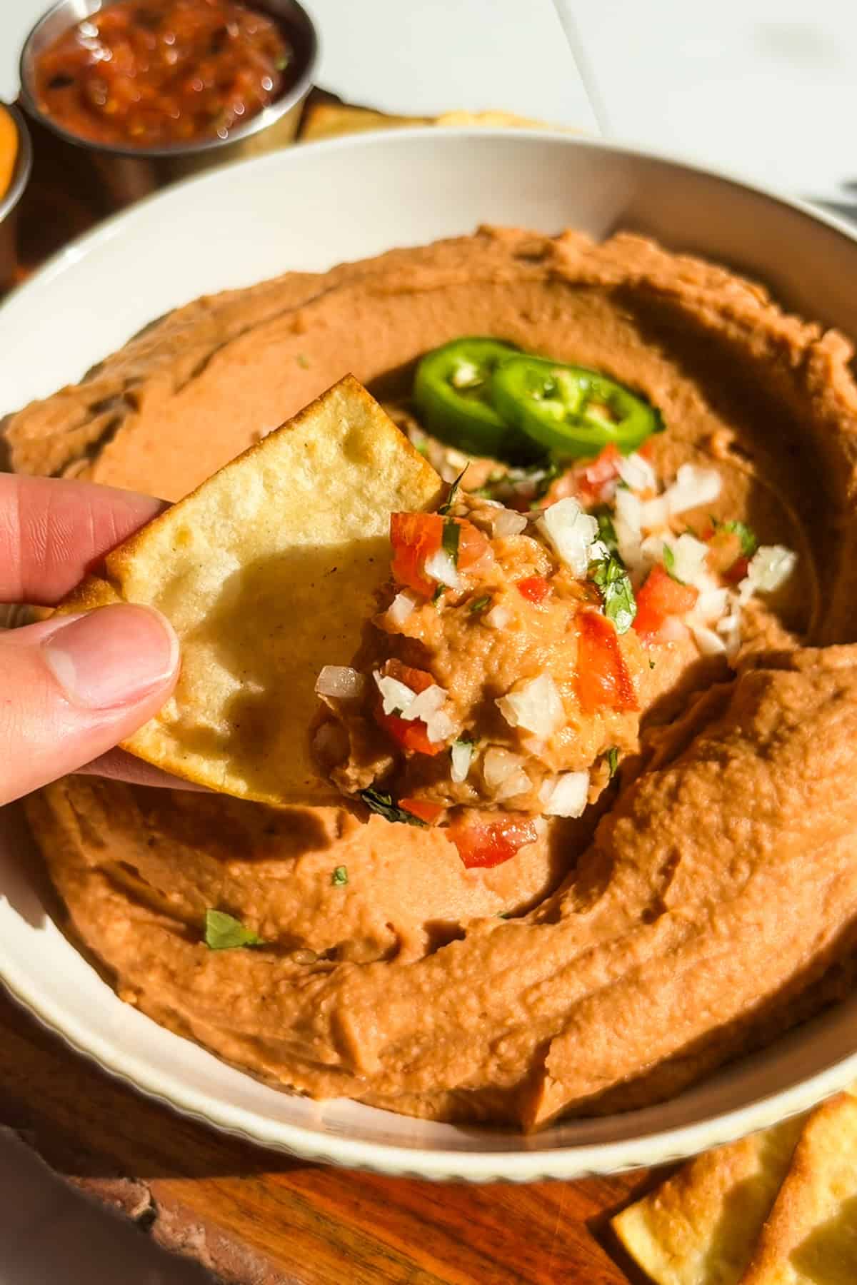 A chip dipping into a white bowl filled with creamy vegan bean dip.