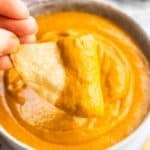 Chip dipping into creamy avocado tomato salsa in a bowl.