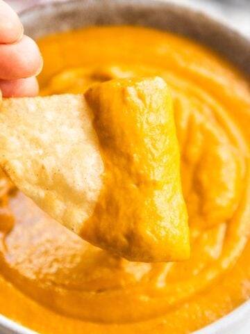 Chip dipping into creamy avocado tomato salsa in a bowl.