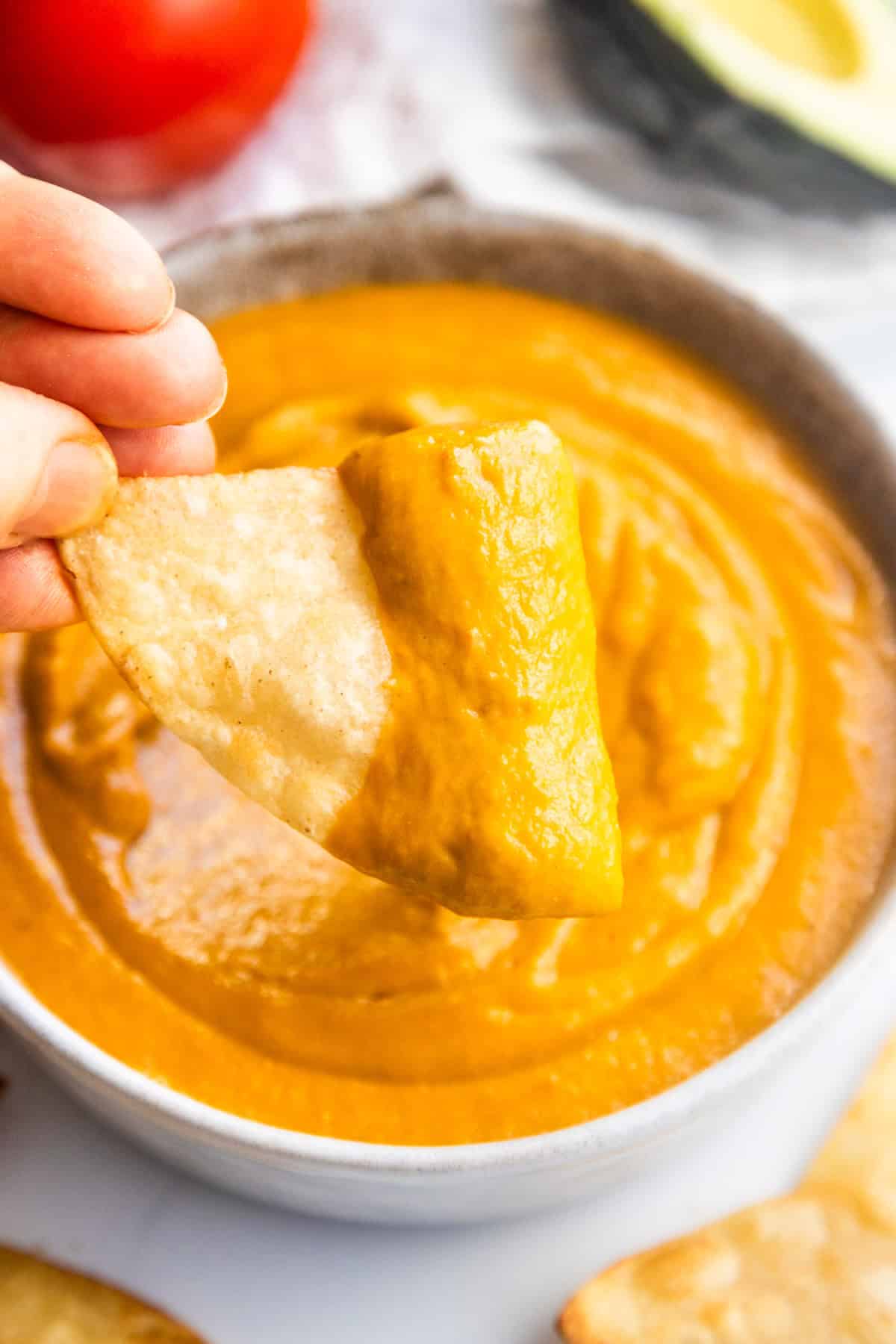 Chip dipping into creamy avocado tomato salsa in a bowl.