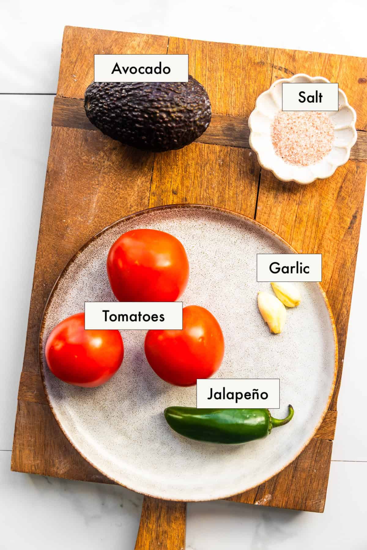 All ingredients for creamy avocado tomato salsa in labeled bowls on a counter.