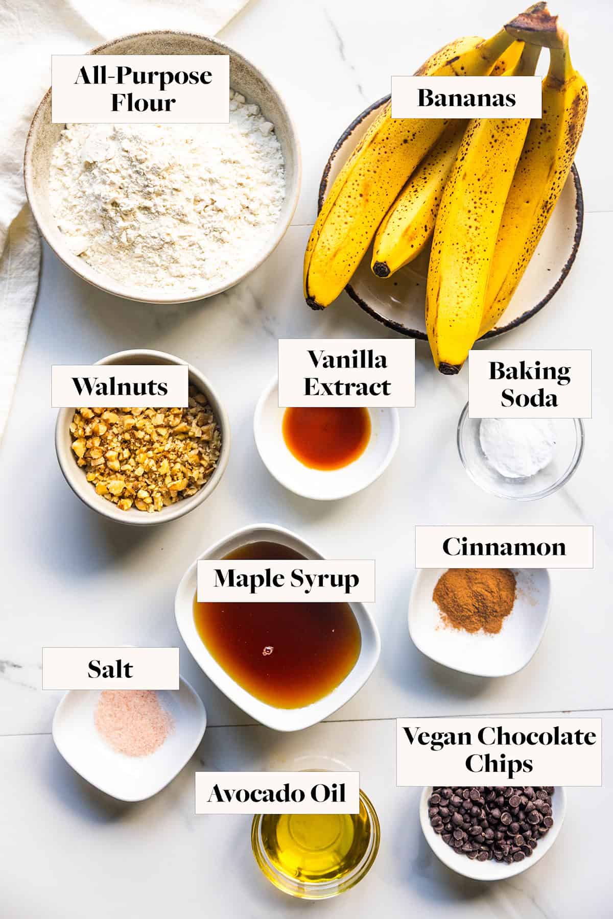 Ingredients for vegan chocolate chip banana bread in labeled bowls.
