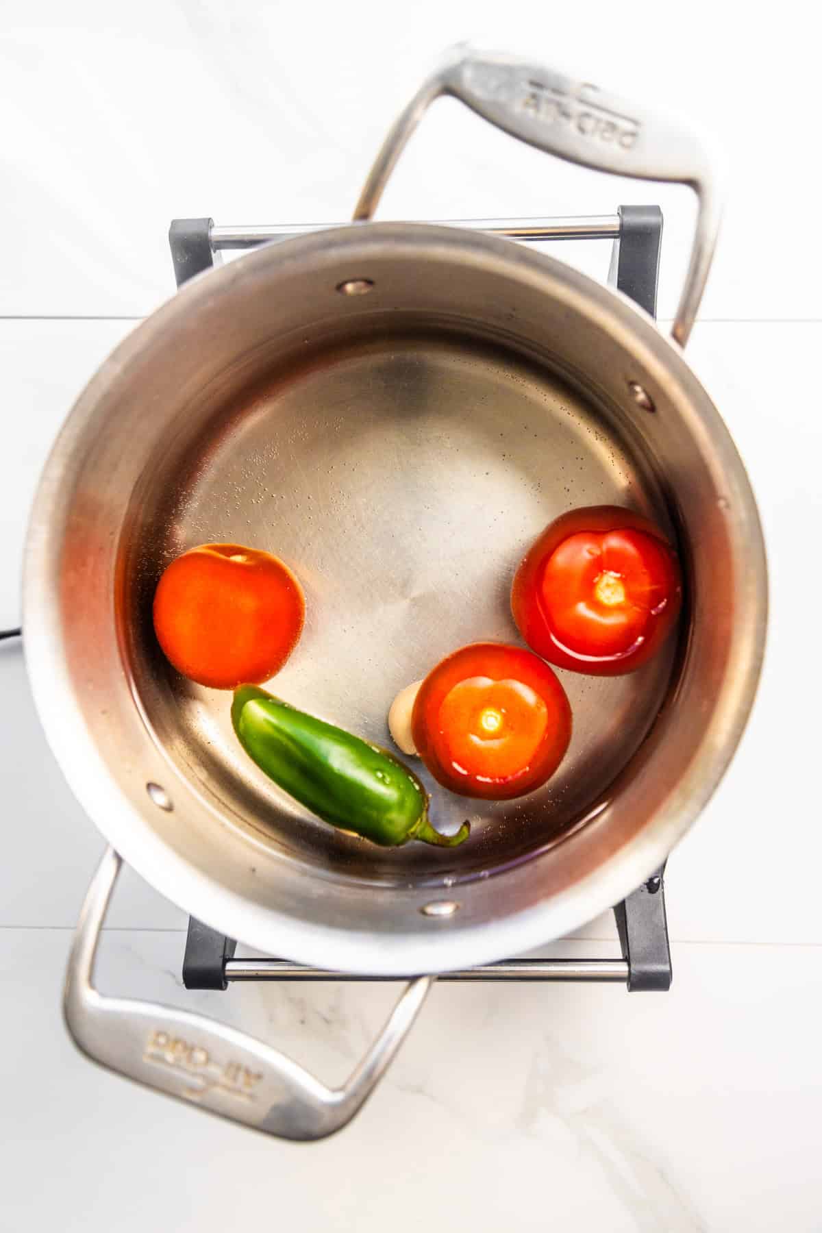 Tomatoes, jalapeños, garlic, and water in a pot.