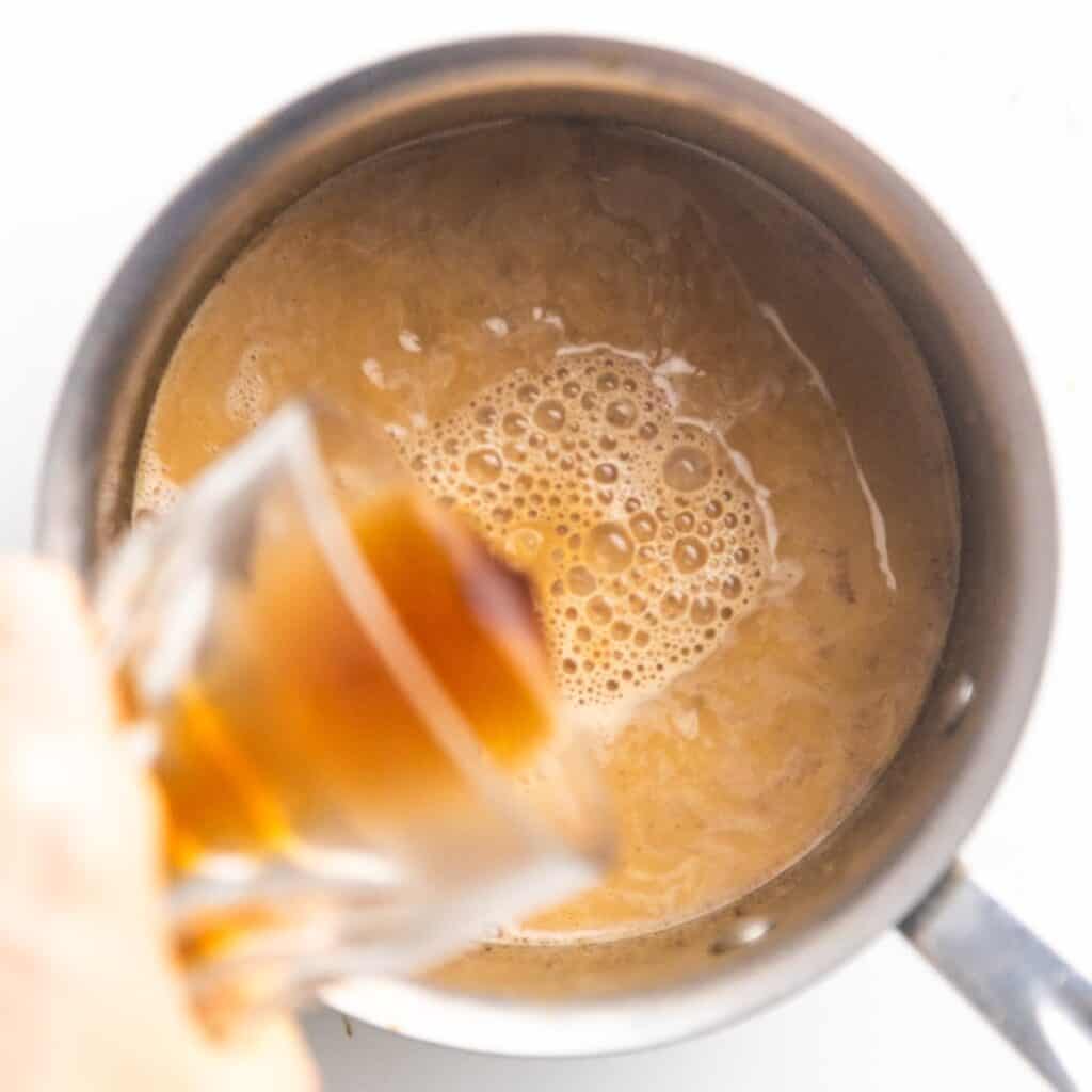 Brewed chai pouring into a saucepan.