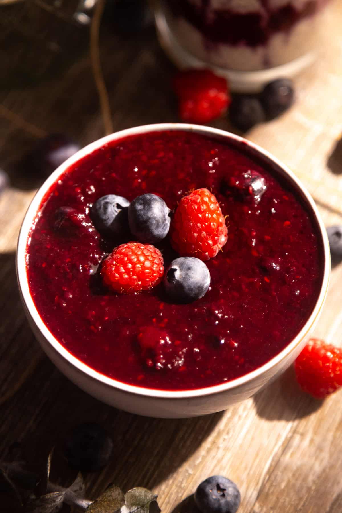 Easy berry sauce recipe in a white bowl topped with fresh berries.
