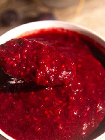Easy berry sauce recipe in a white bowl with a spoon dipping in.
