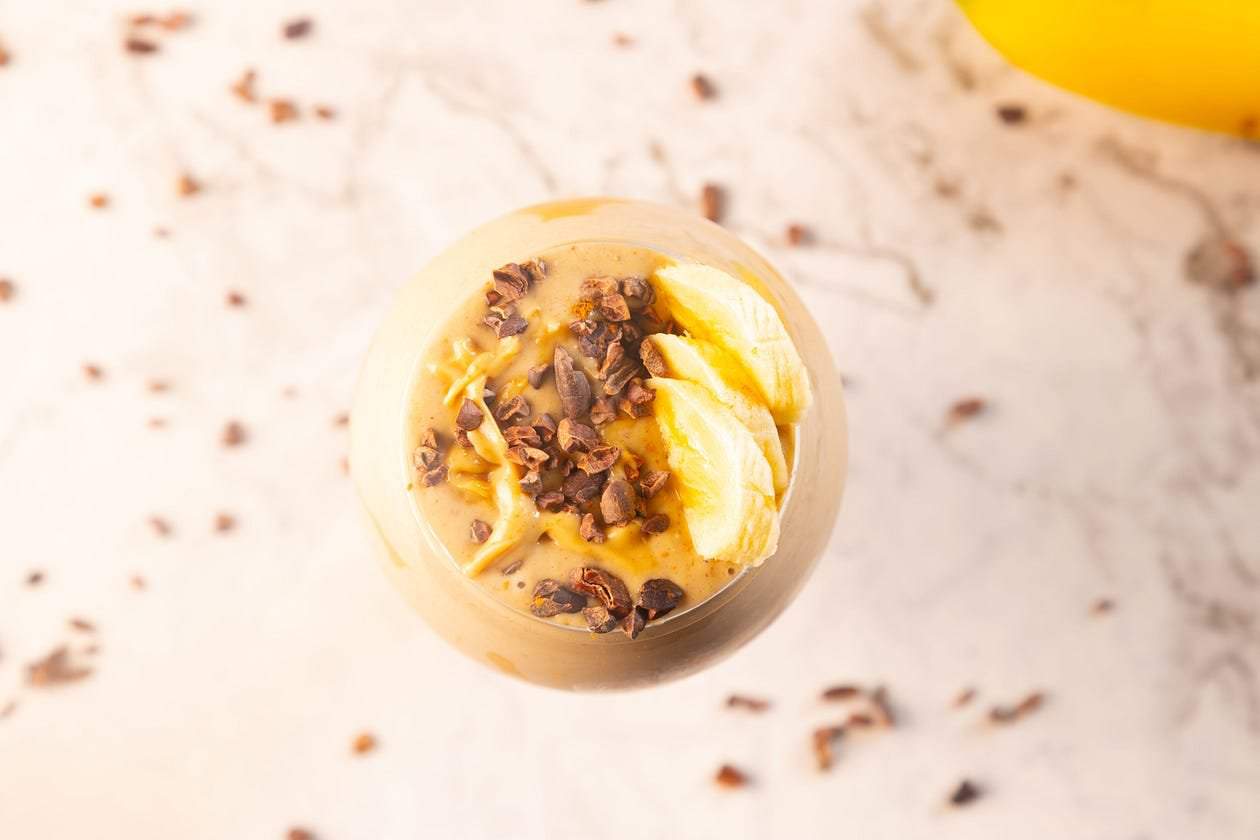 Banana peanut butter smoothie in a glass topped with sliced bananas and cacao nibs.