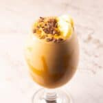Peanut butter smoothie recipe in a glass topped with cacao nibs, sliced bananas, and creamy peanut butter.