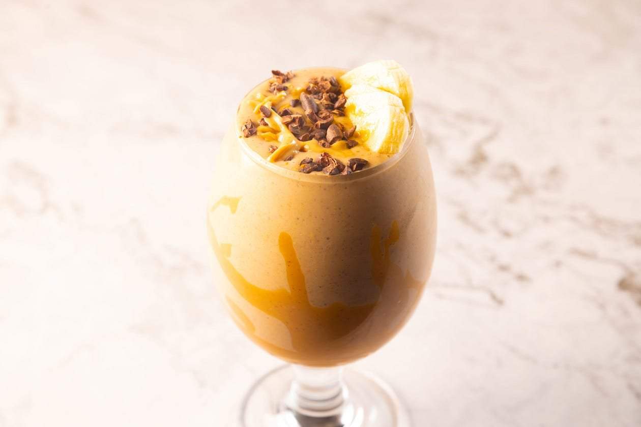Peanut butter smoothie recipe in a glass topped with cacao nibs, sliced bananas, and creamy peanut butter.