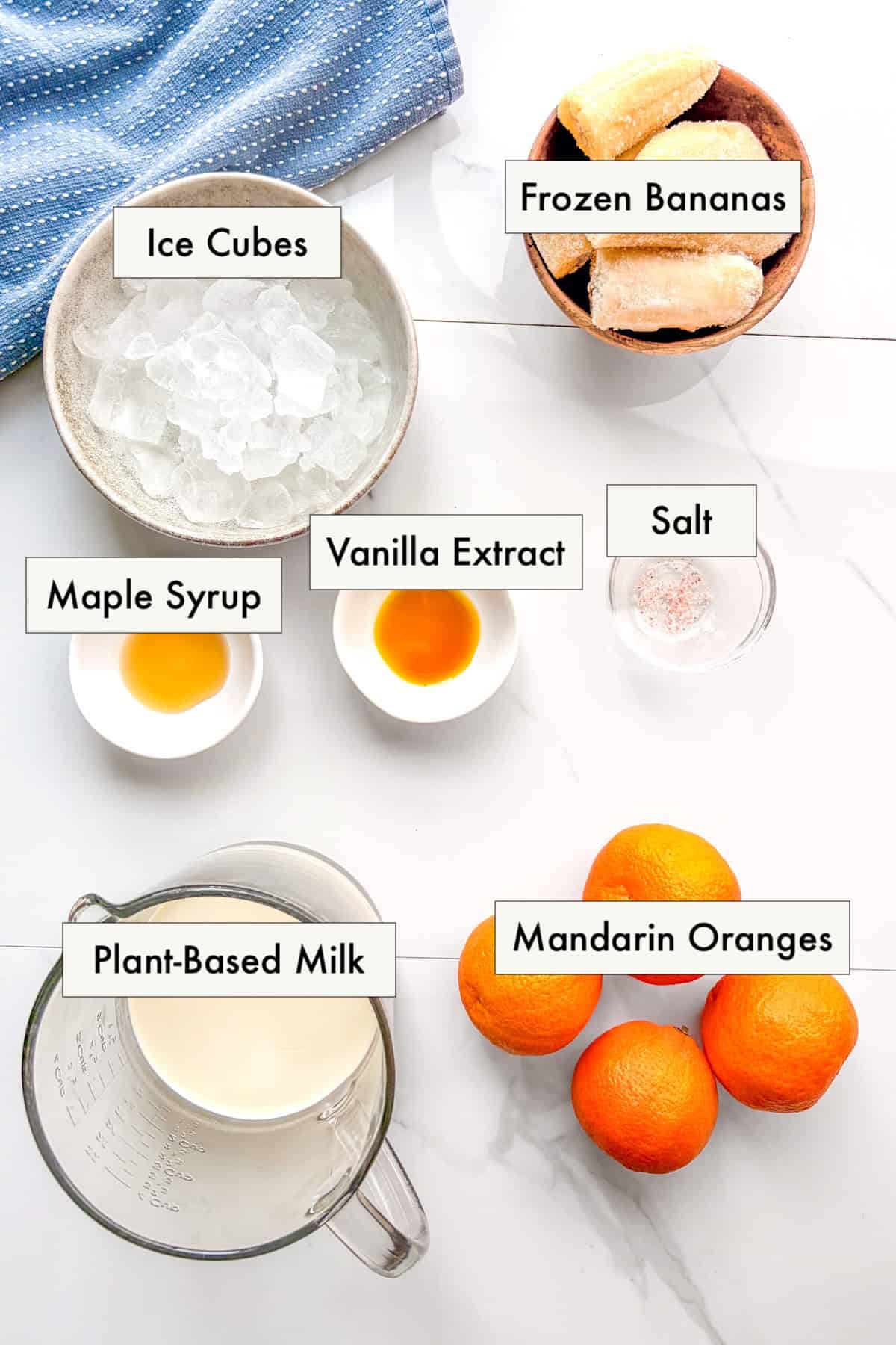 All ingredients for dairy-free orange creamsicle smoothie in labeled bowls on a counter.