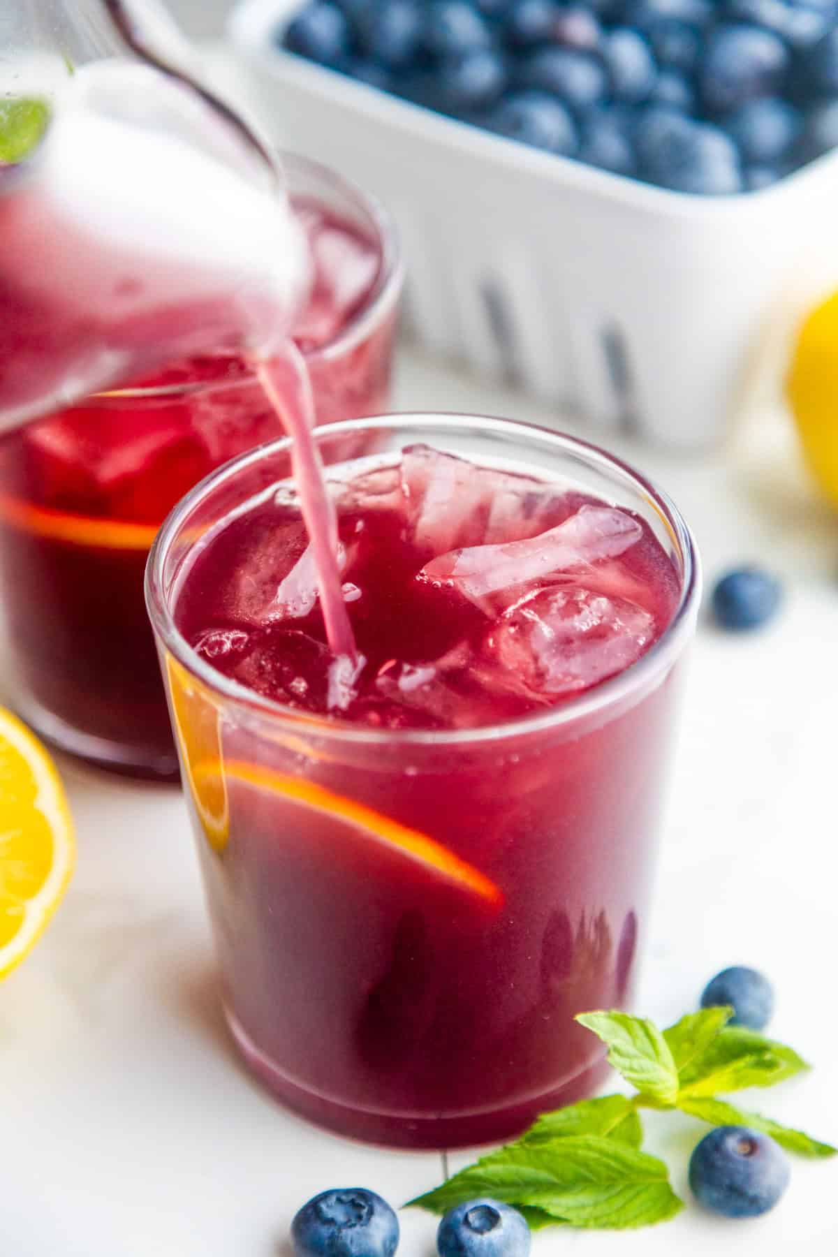 Easy blueberry lemonade recipe pouring into a glass.