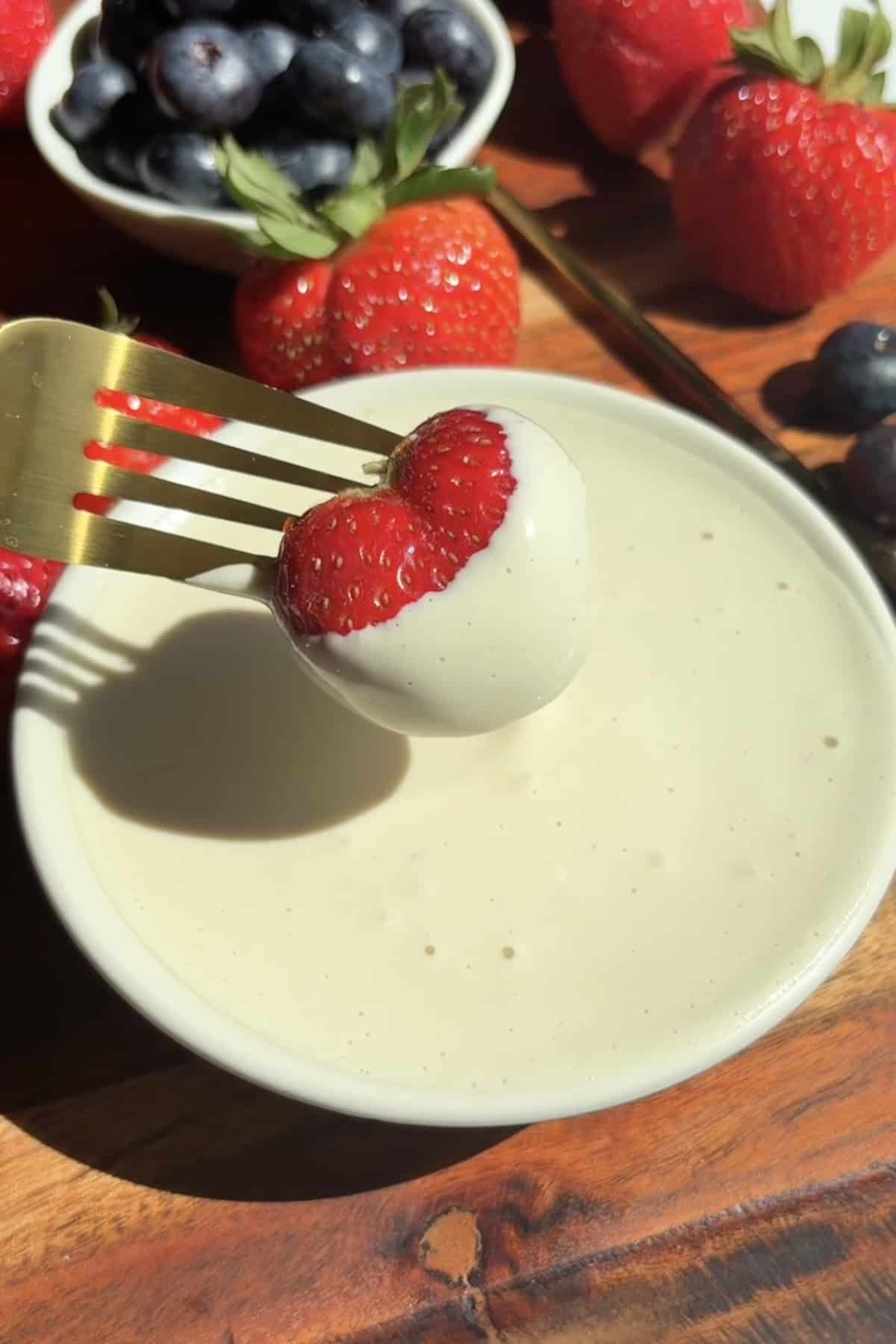 Strawberry dipping into a bowl of healthy vegan fruit dip.