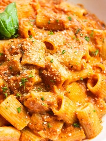 Vegan pink pasta served on a white plate, topped with fresh basil leaves and vegan parmesan.