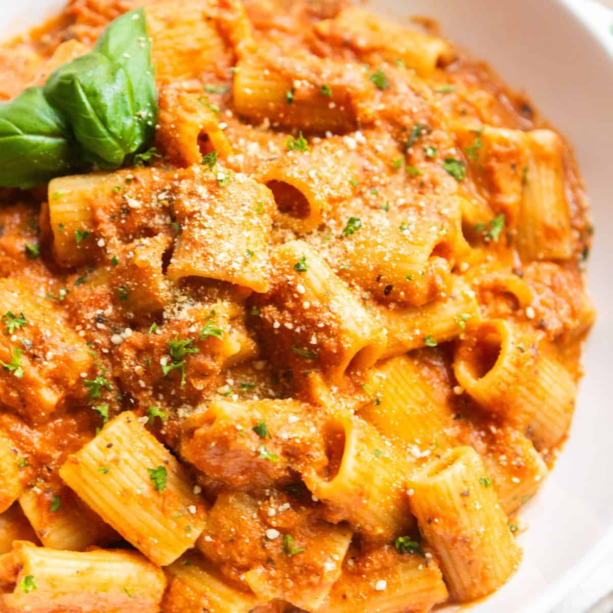 Vegan pink pasta served on a white plate, topped with fresh basil leaves and vegan parmesan.