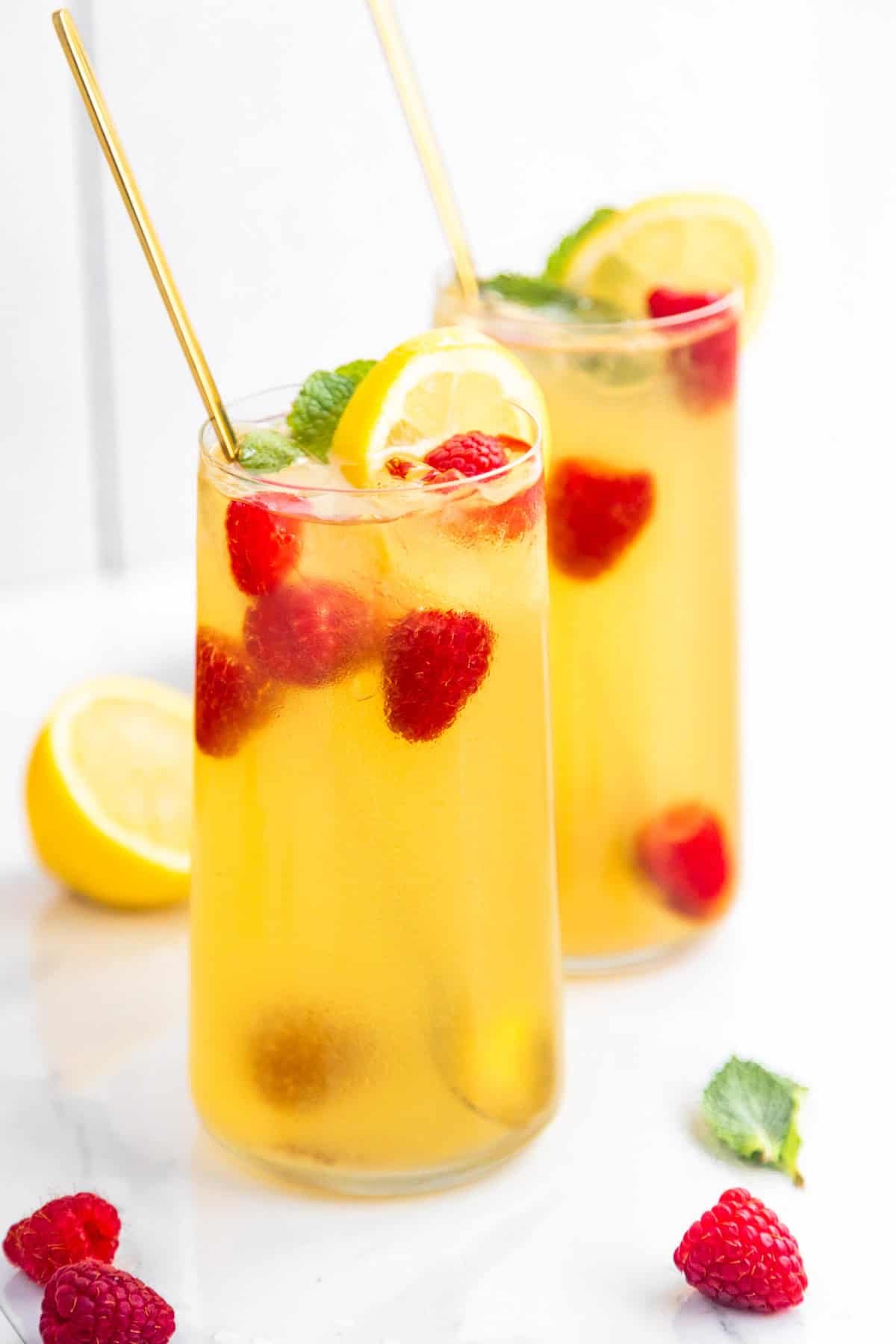 Glasses of iced green tea with raspberries and lemon, with mint and fruit on the side.
