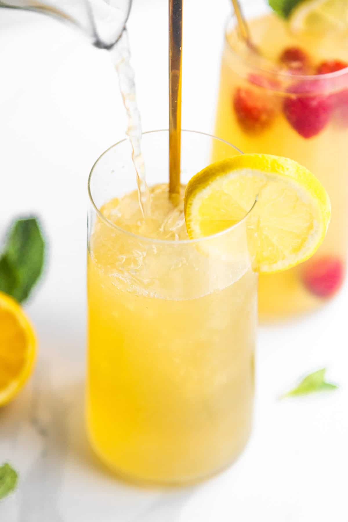 Green tea lemonade pouring into a glass with ice cubes and lemon wedges.