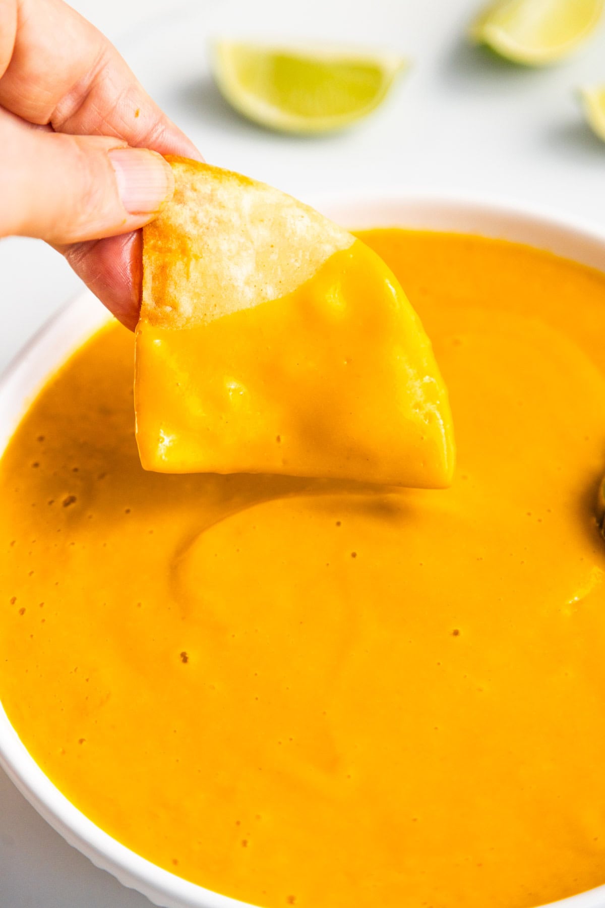 Homemade tortilla chip dipping into a bowl with vegan nacho cheese sauce.