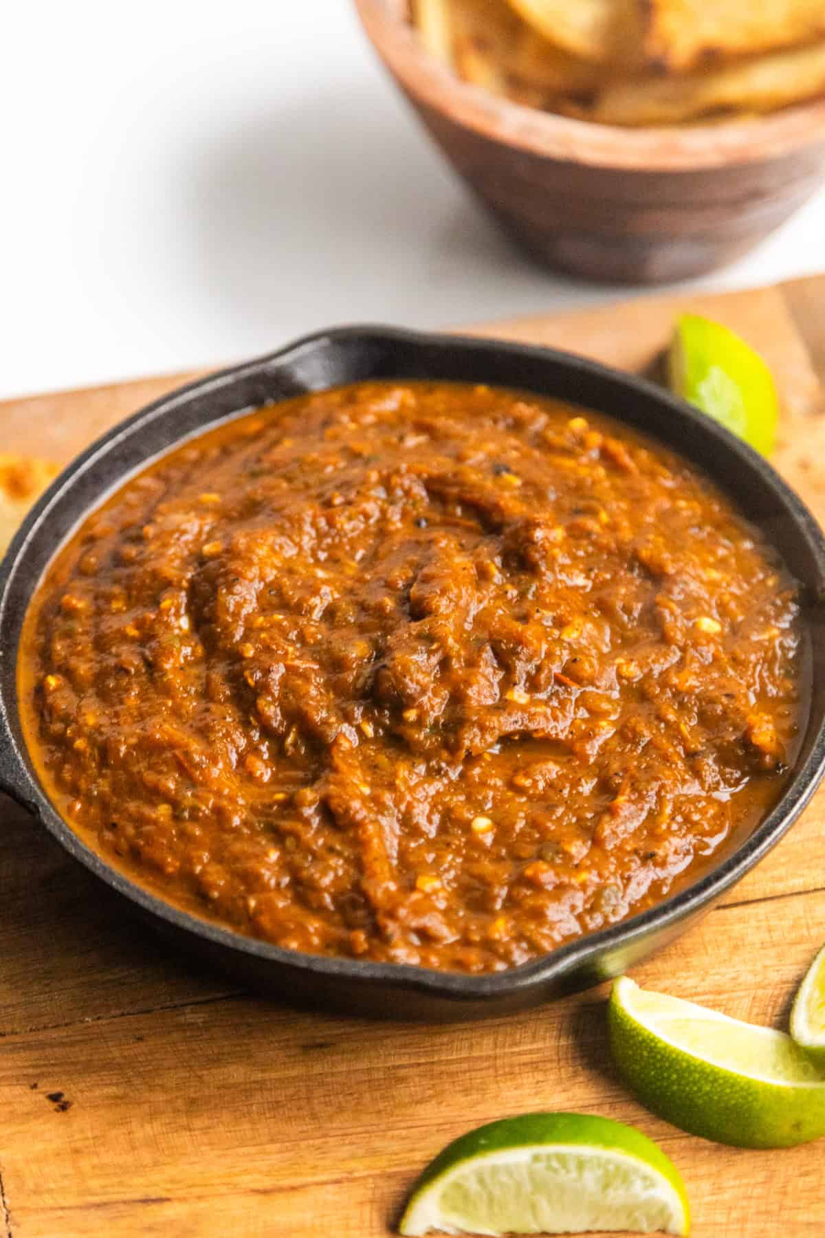 Roasted red salsa in a cast iron skillet with lime wedges on the side.