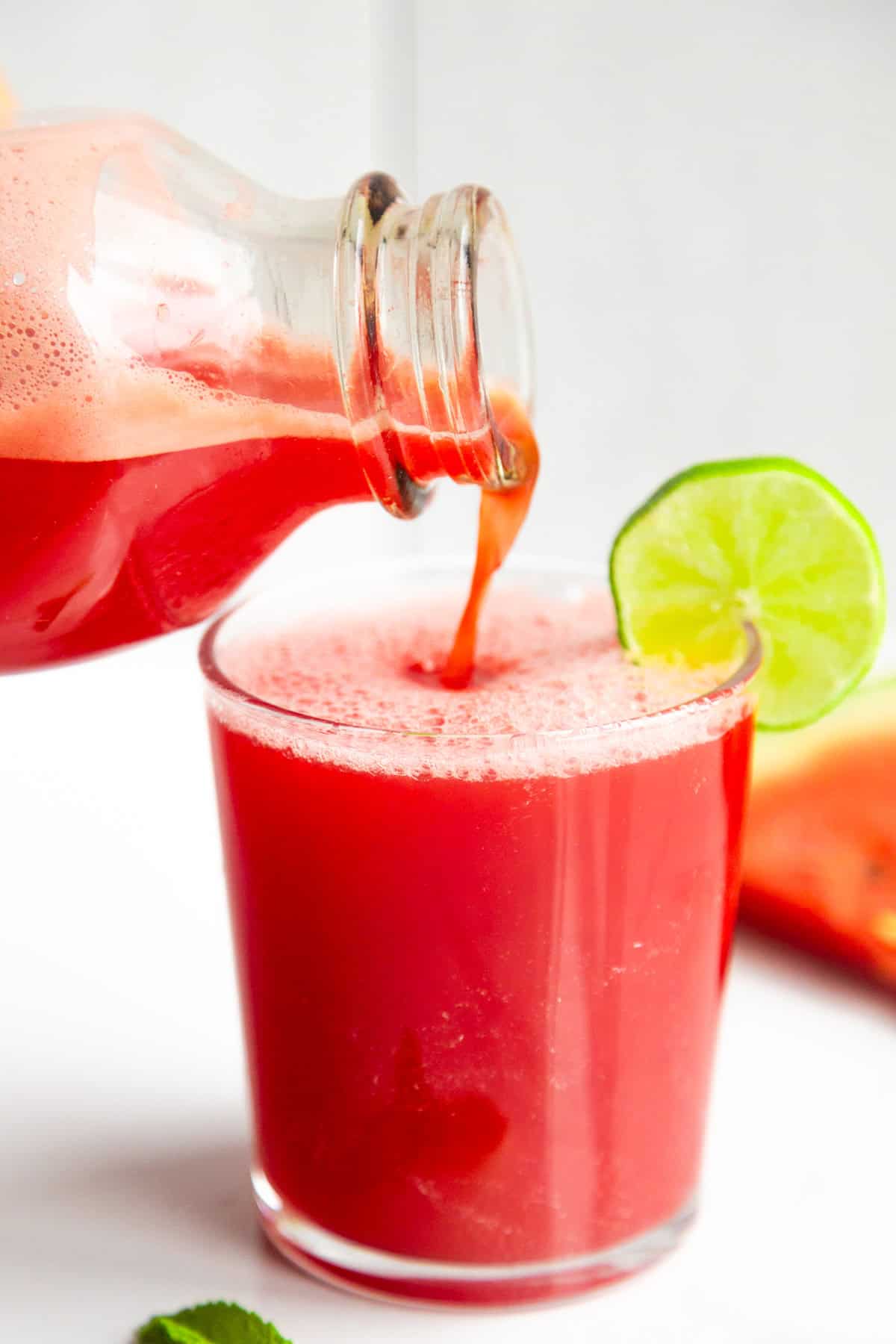 Watermelon juice pouring into a glass with a lime wedge.