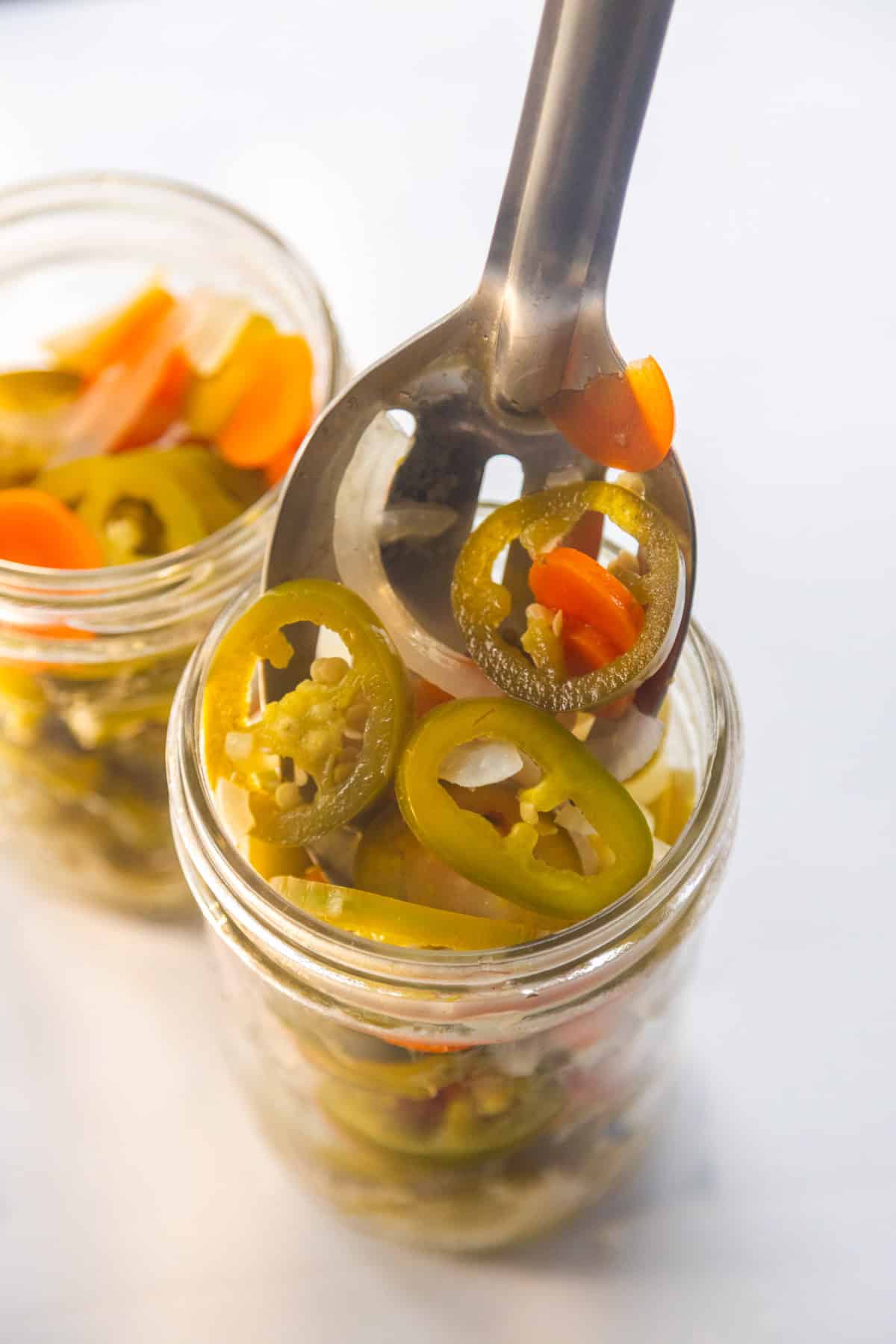 Jalapeños carrots and onions being scooped into mason jars.