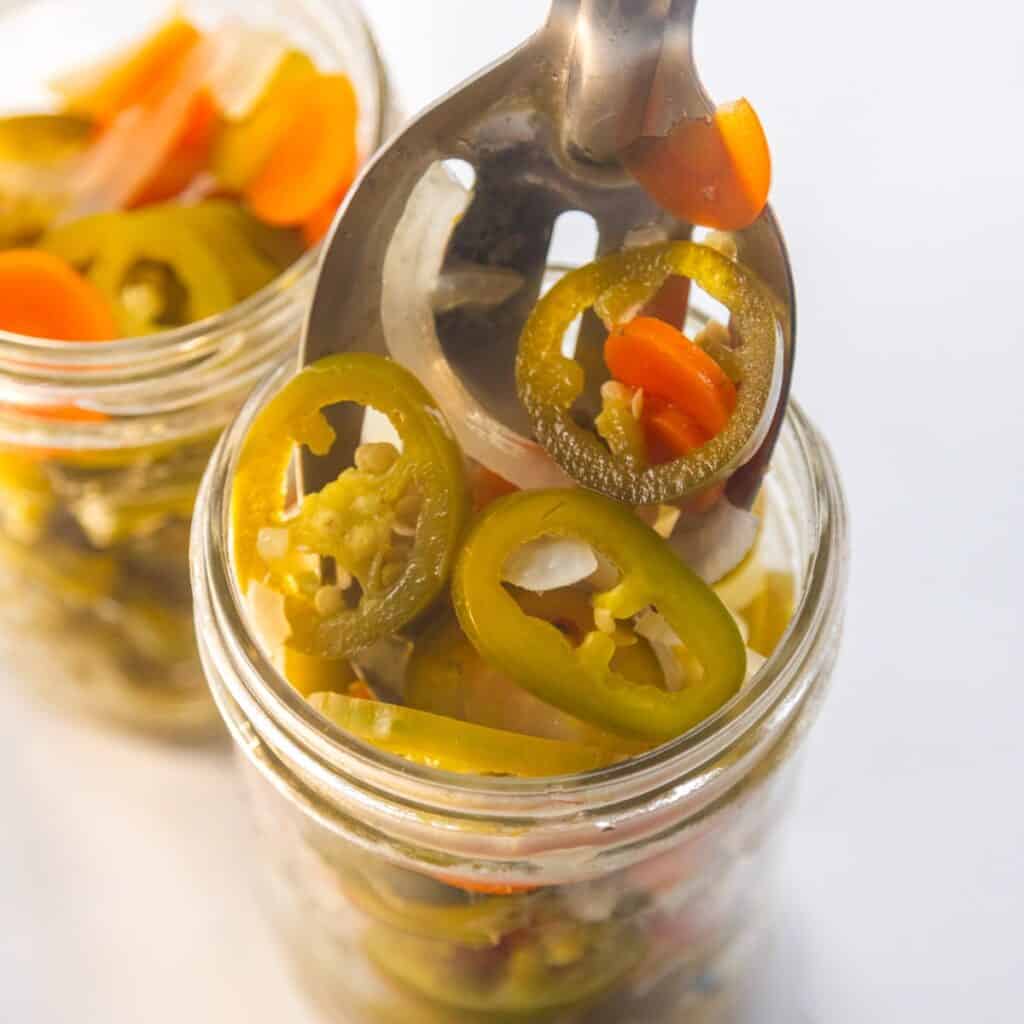 Pickled jalapeños being scooped into a mason jar.