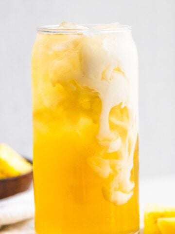 Pineapple skin tea in a glass with a splash of oatmilk.