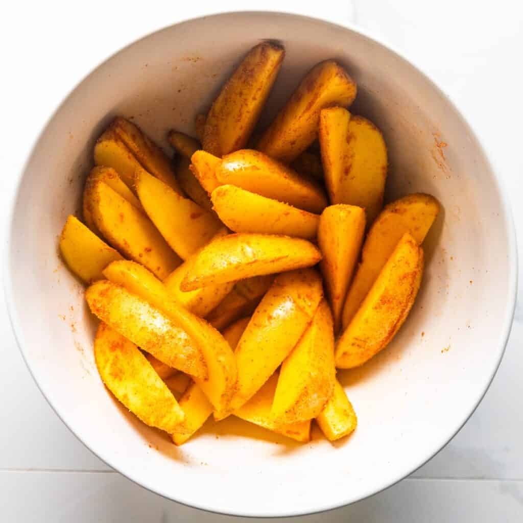 Potato wedges in a bowl mixing with seasonings.