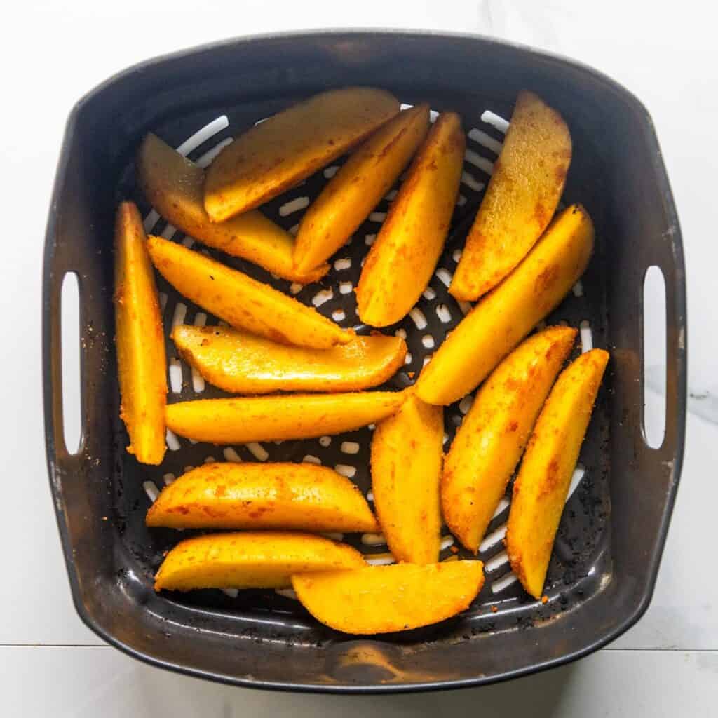 Potato wedges in an air fryer basket preparing to cook.