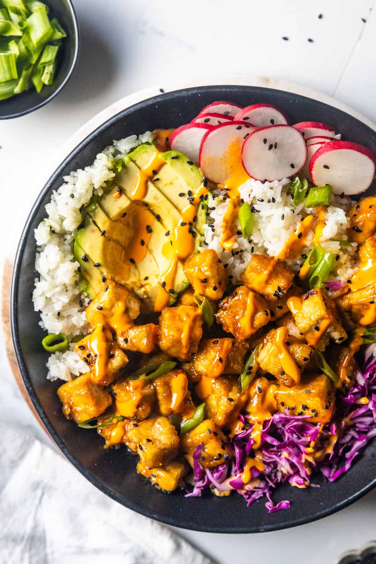 Overhead shot of a tofu bowl with maple glazed tofu, rice, avocado, radishes, and purple cabbage, drizzled over with chipotle sauce.